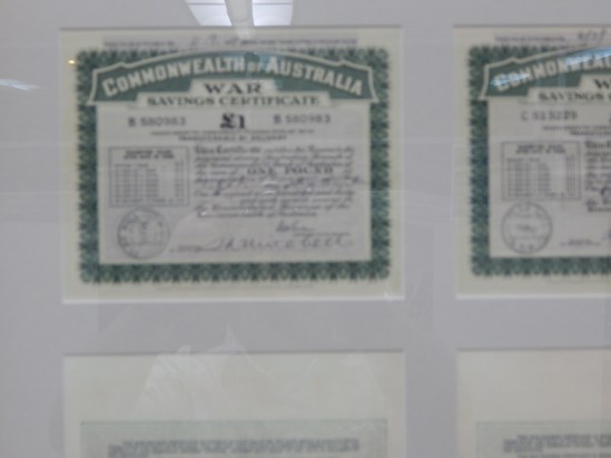 A copy of a War Savings Certificate that was issued in Peak Hill. There are two in the display and both were kindly donated to Parkes Shire Library by Joyce Stanford and Judy Barter. War Savings Certificates were a way for the Australian Government to raise much needed funds to support the war, and also for people unable to fight to contribute to the war effort. The best way to explain the concept of a war savings certificate to a younger audience is this - it's like a gift card but with compound interest. These War Savings Certificates were purchased in 1940 for 16 shillings (16s 0d) which is approximately $1.60 in today's currency. After seven years the certificate could be exchanged at the bank of issue for cash - these certificates are for one pound (£1) or approximately $2 today (source Reserve Bank of Australia Pre-decimal Inflation Calculator <a href=