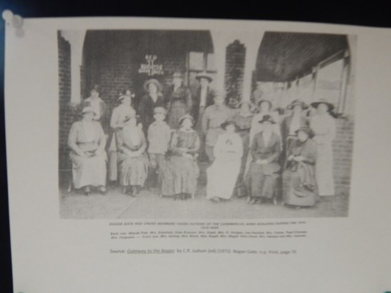 Photograph of Bogan Gate Red Cross members taken outside of the Commercial Bank Building during the 1914-1918 War Back row (left to right): Maude Pett, Mrs Schofield, Elsie Rowson, Mrs Stack, Mrs R Hodges, Joe Haylock, Mrs Coster, Pearl Coombs, Mrs Ferguson, ?. Front row: Mrs Solling, Mrs Black, Mac Magill, Mrs Magill, Kitty Hood, Mrs Herbert and Mrs Coombs. Photograph is from Gateway to the Bogan by C R Judson (Editor) and Parkes Shire Library has two copies - one of public catalogue for borrowing and another reference copy in the Family & Local History room.