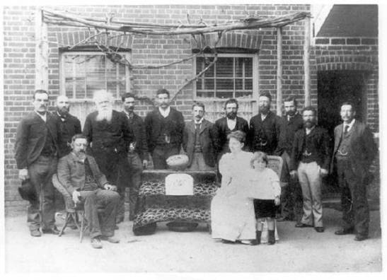Photograph of Henry Parkes on one of his many visits to the Shire that would one day bear his name. The sign in front of the gold (now faded) originally read 'New Bushman's Hill Tribute - Parkes. "The Lady Parkes" 1347 oz' In this photograph (standing, left to right) T Faull, J Mackay, Sir Henry Parkes, D Jones, H Ensor, Albert William Buzzacott (local manager of the Bank of Australasia), R Copp, M Fifield, J Warn, J Faull, HS Harwood, (sitting) R Wright (Mine Manager), Lady Eleanor Parkes and son Charles Henry. Source: Parkes: A Photographic History by Ian Chambers, 1988 Self-published: Parkes, NSW page 45