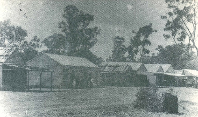 Reproduction of a photograph of the main street in Alectown in 1893. The view is looking north. This photograph is on the back cover of one of Len Unger's historical booklets. The buildings are (from left to right) Barnett's Butchery, McGee and Quinn's Bakery, Bark Shop, Foster's Original Store, Club House Hotel (with double gables), Bark Building used for school purposes in 1890, Miner's Exchange Hotel, Fletcher's Billiard Saloon. Source: Unger, L. A. (1983). Stories of Alectown: historical - humorous - tragic Parkes, N.S.W.: Parkes & District Historical Society